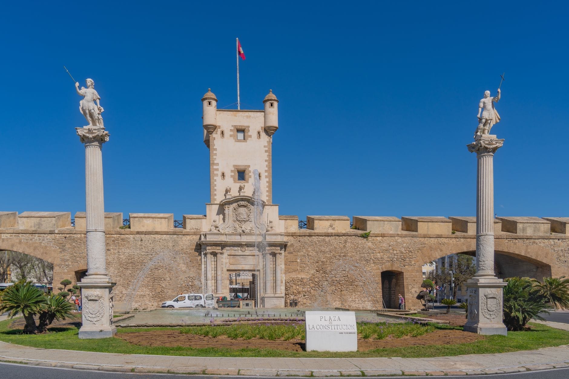 Kuleler ve heykellerle süslü taş şehir kapısı, Plaza de la Constitución, İspanya'nın Cádiz şehrinde açık mavi gökyüzünün altında.