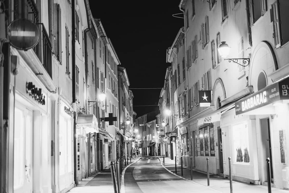 Czarno-białe zdjęcie Rue d'Antibes w Cannes nocą, otoczonej butikami, sklepami i delikatnie oświetlonymi witrynami.