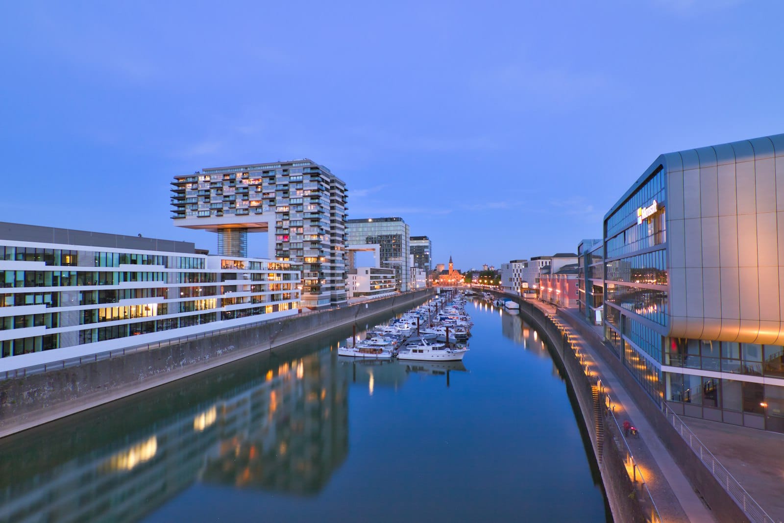 อาคารสมัยใหม่ของ Rheinauhafen เมือง Cologne สะท้อนในคลองท่าเรือยามพลบค่ำ พร้อมหอคอย Kranhaus และมารีนาที่มองเห็นได้