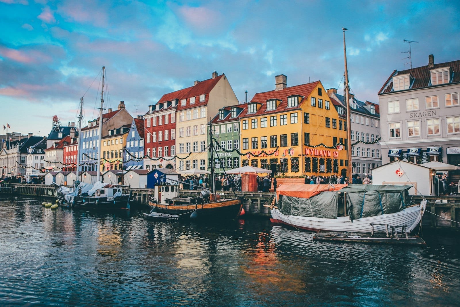 Os coloridos prédios do porto de Nyhavn refletidos no canal ao pôr do sol, com barcos ancorados e um céu vibrante — o cartão-postal de Copenhague.