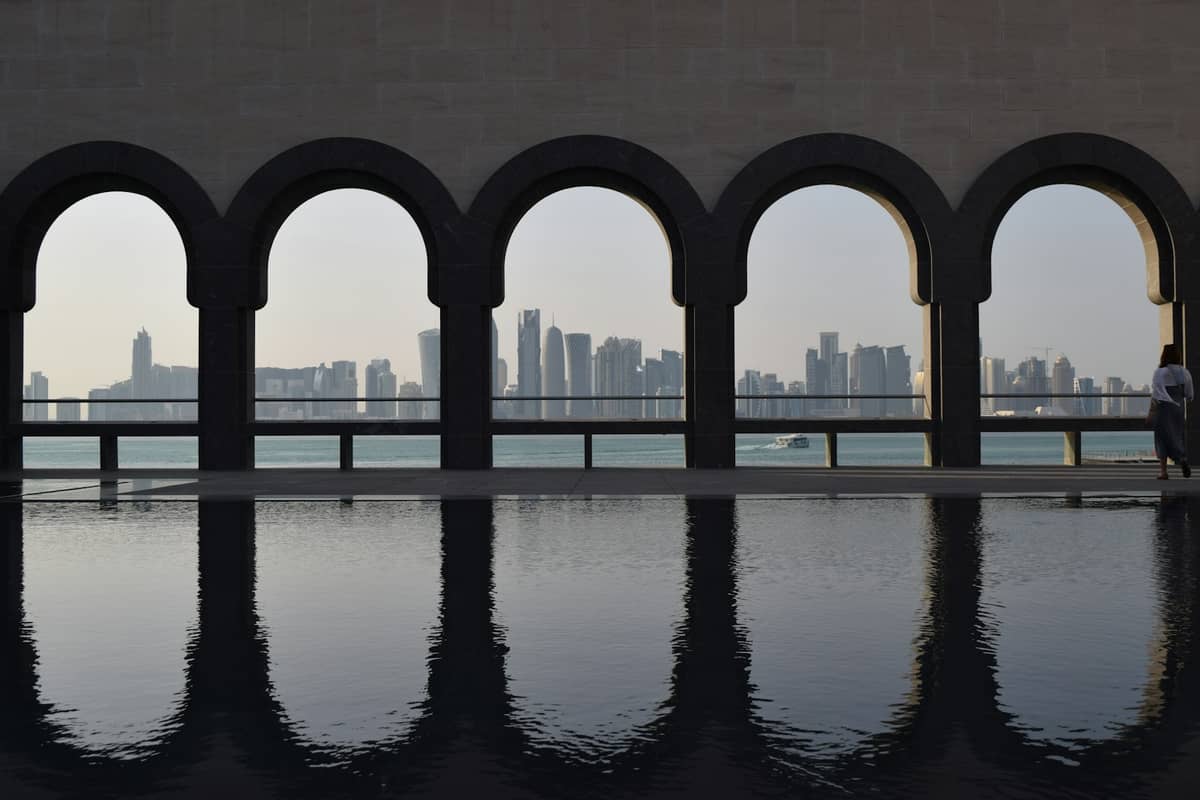 Blick auf die Skyline von Doha über die Bucht, gerahmt von den Bögen des Museums für Islamische Kunst mit Wasserspiegelung im Vordergrund.