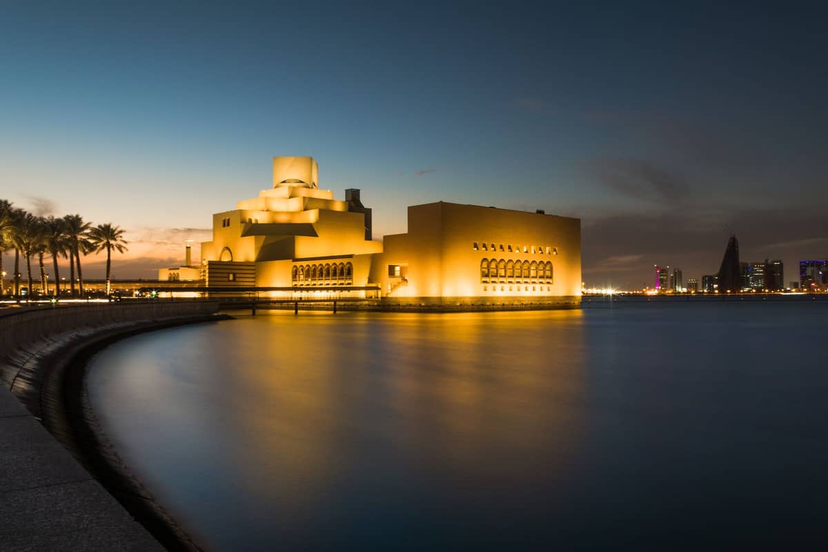 Das Museum für Islamische Kunst in Doha in der Abenddämmerung beleuchtet, von der Corniche aus mit der Skyline der Stadt im Hintergrund gesehen.