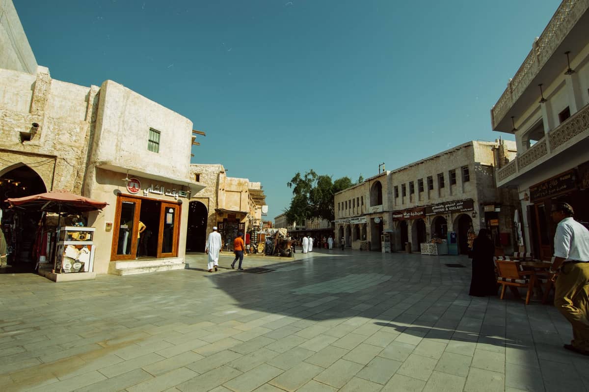 Offener Platz im Souq Waqif in Doha, gesäumt von Restaurants und traditionellen Gebäuden, Menschen schlendern und speisen im Freien unter blauem Himmel.