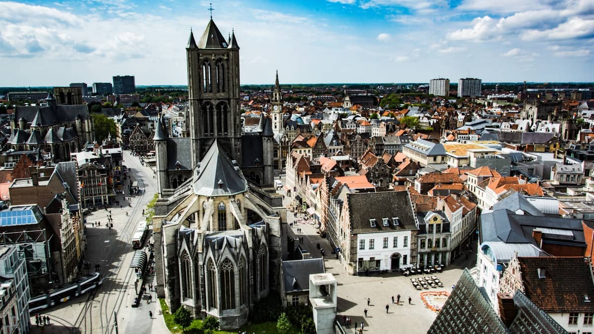 Aerial view of Ghent’s medieval city center with Saint Bavo's Cathedral and historic buildings under a blue sky.
