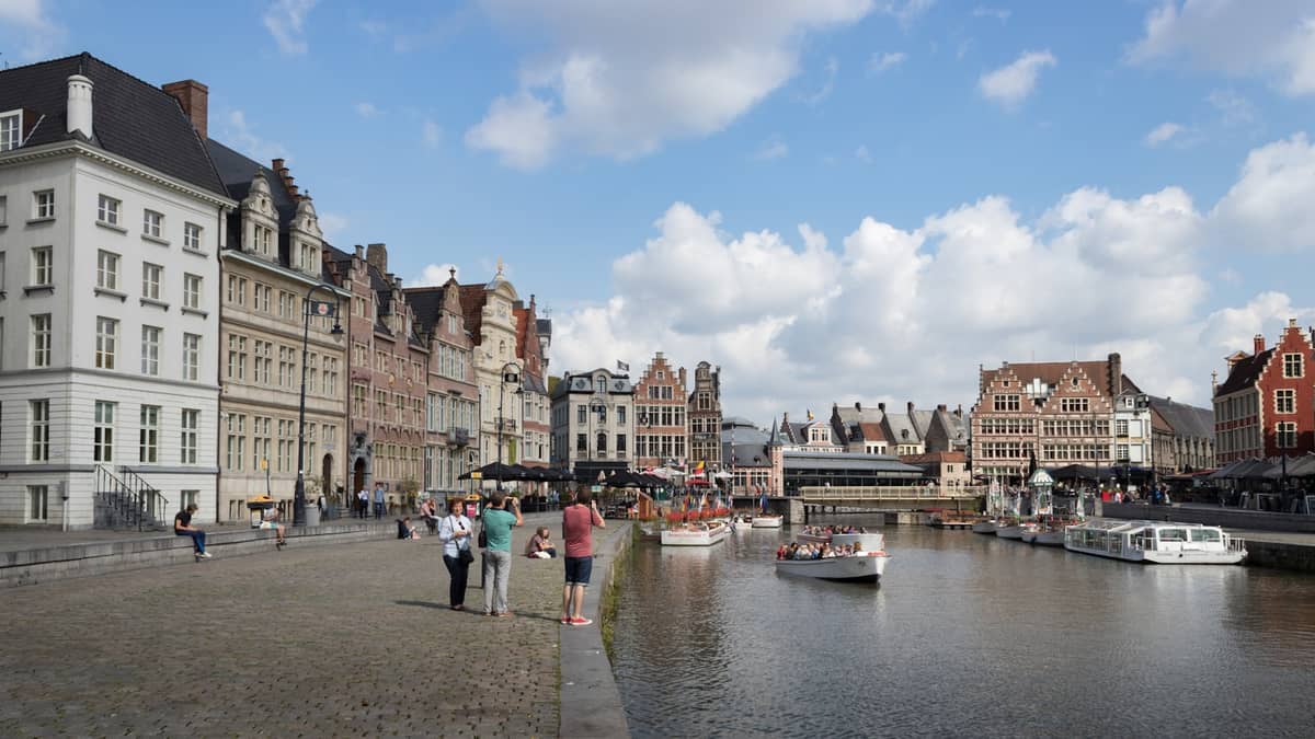 View of Ghent's Graslei and Korenlei canal, with historic medieval guild houses and tour boats on a sunny day.