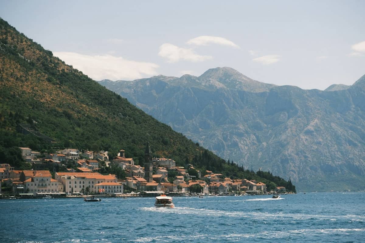 View from the water of a boat on the Bay of Kotor, with red-roofed buildings and steep mountains in the background.