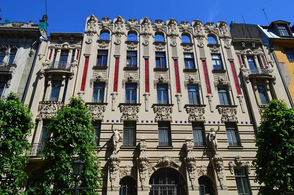 Prachtvolles Jugendstilgebäude an der Alberta iela in Riga, mit gemeißelten Gesichtern und Figuren an der Fassade vor blauem Himmel.