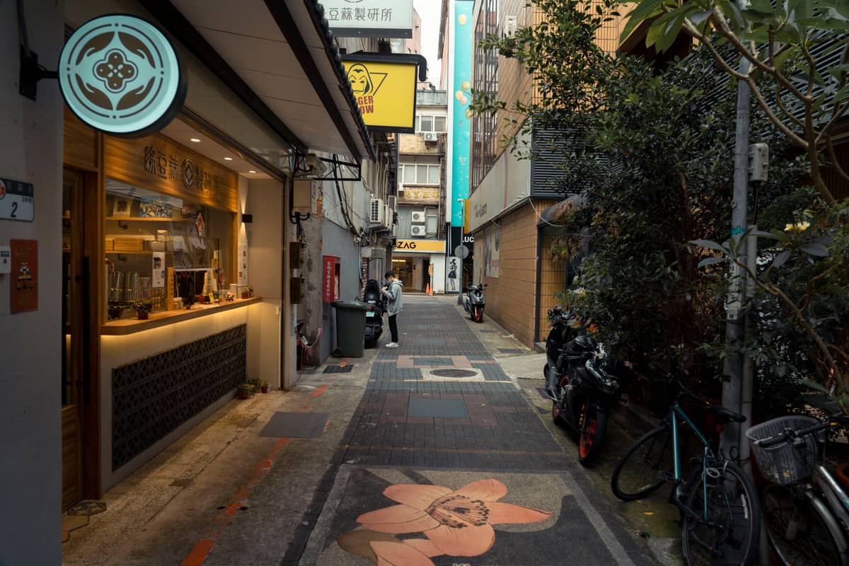Beco urbano estreito em Shenzhen com lojas locais, bicicletas e letreiros, sugerindo oportunidades para experiências locais únicas adicionais.
