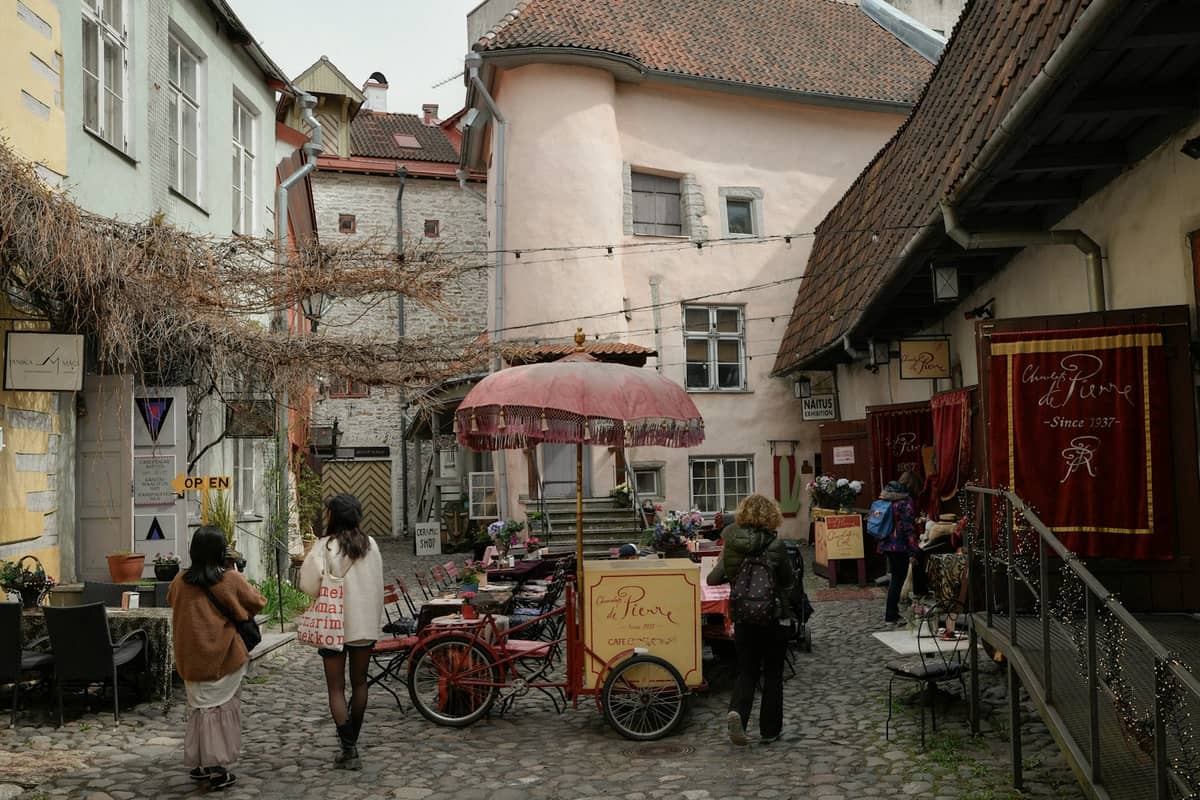 Kopfsteinpflaster-Gasse im mittelalterlichen Tallinn Old Town mit bunten Gebäuden, kleinen Geschäften, Café-Tischen im Freien und Fußgängern, die durch die stimmungsvolle Passage schlendern.