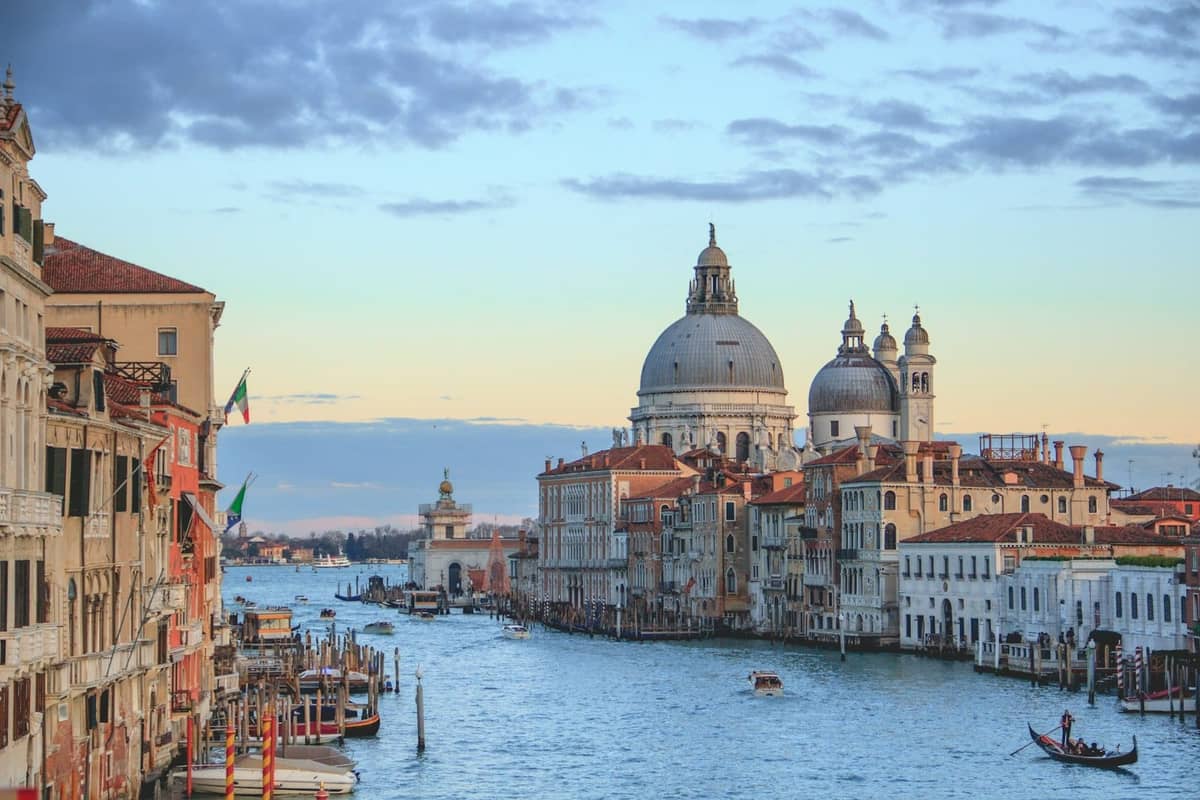 Klassischer Blick den Canal Grande hinunter bei Sonnenuntergang in Venedig, mit der Kirche Santa Maria della Salute im Hintergrund und Booten auf dem Wasser.