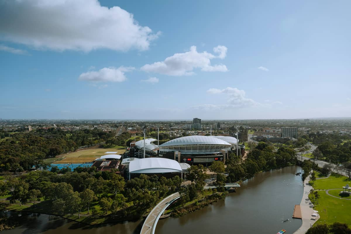 Luftaufnahme der Innenstadt von Adelaide mit dem Adelaide Oval Stadion, Parklandschaften, Fluss und Stadtpanorama unter blauem Himmel.