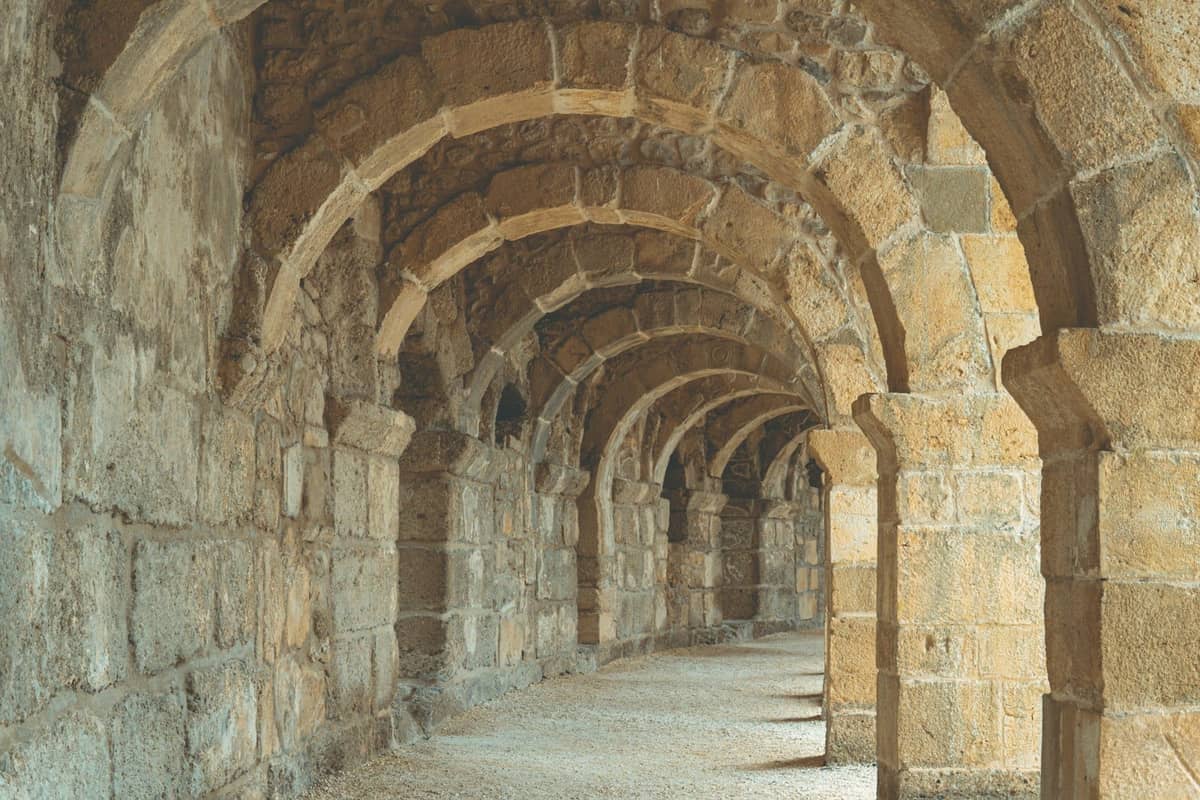 Series of ancient stone arches forming a vaulted corridor, likely part of Perge's Roman-era ruins near Antalya.