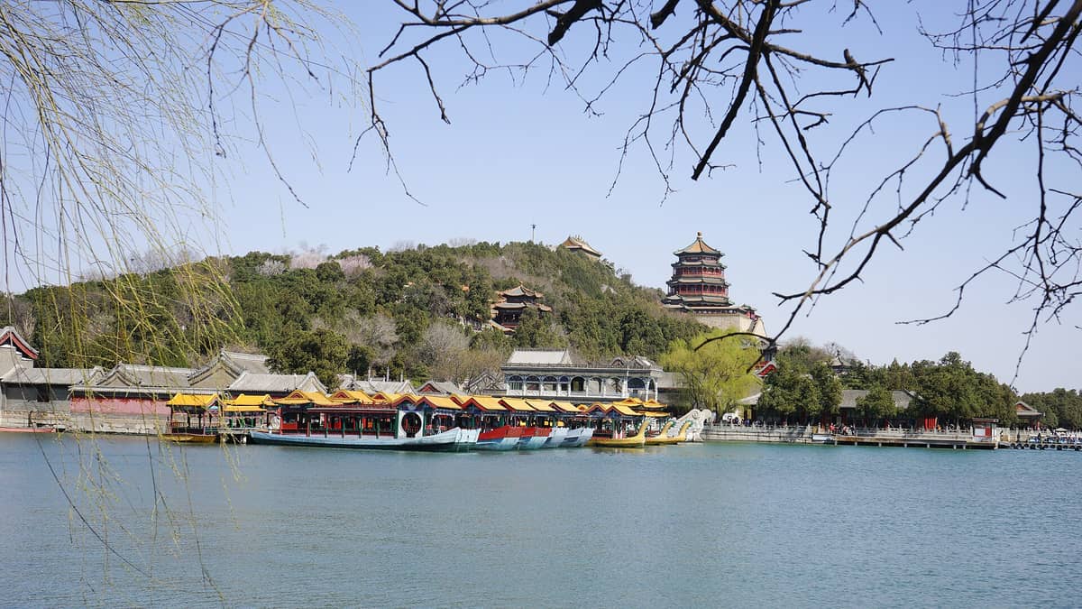 Weitwinkelansicht des Sommerpalastes in Peking mit bunten Booten auf dem See, dem Hügel der Langlebigkeit und verzierten Pavillons unter klarem Himmel.