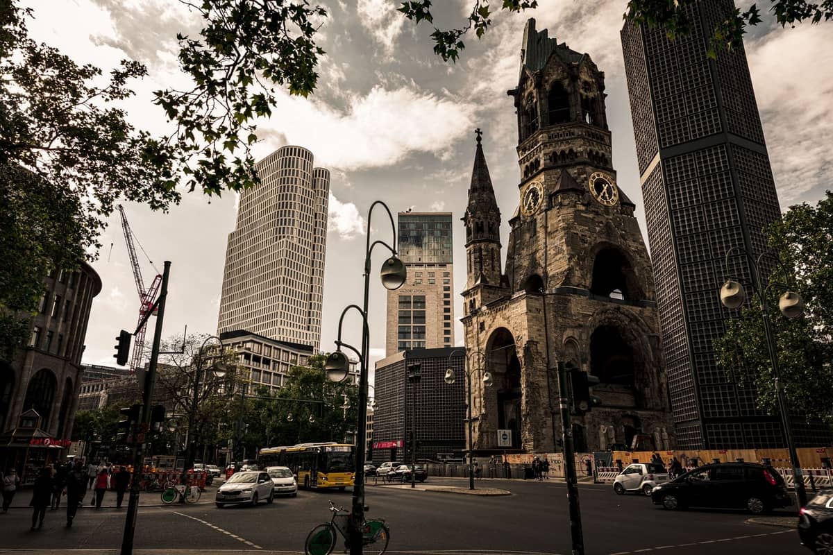 Vista amplia de la Kaiser Wilhelm Memorial Church y el paisaje urbano circundante del Berlín Occidental con personas, tráfico y edificios modernos.