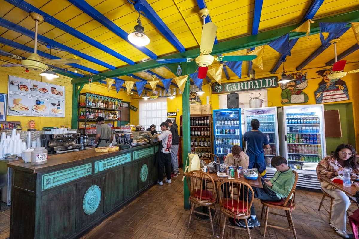 Colorful, bustling café interior with people eating and drinking, yellow and blue ceiling, and a lively local atmosphere.