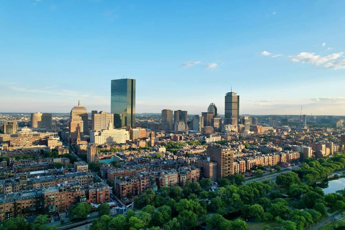 Widok z lotu ptaka na centrum Bostonu z zielonymi parkami, historycznymi budynkami z cegły i nowoczesnymi wieżowcami pod bezchmurnym błękitnym niebem.