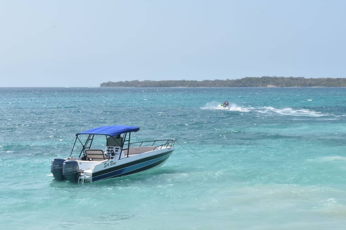 A small motorboat with a blue canopy floating on clear turquoise water near a distant island, evoking Caribbean island-hopping.