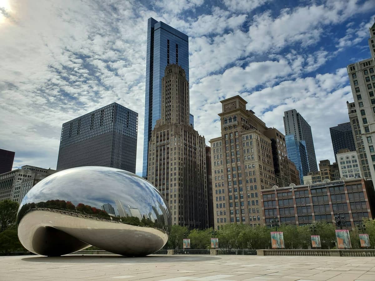 Ein klarer Blick auf das Cloud Gate (die Bohne) im Millennium Park Chicago, mit Wolkenkratzern der Stadt im Hintergrund unter einem blauen Himmel mit vereinzelten Wolken.