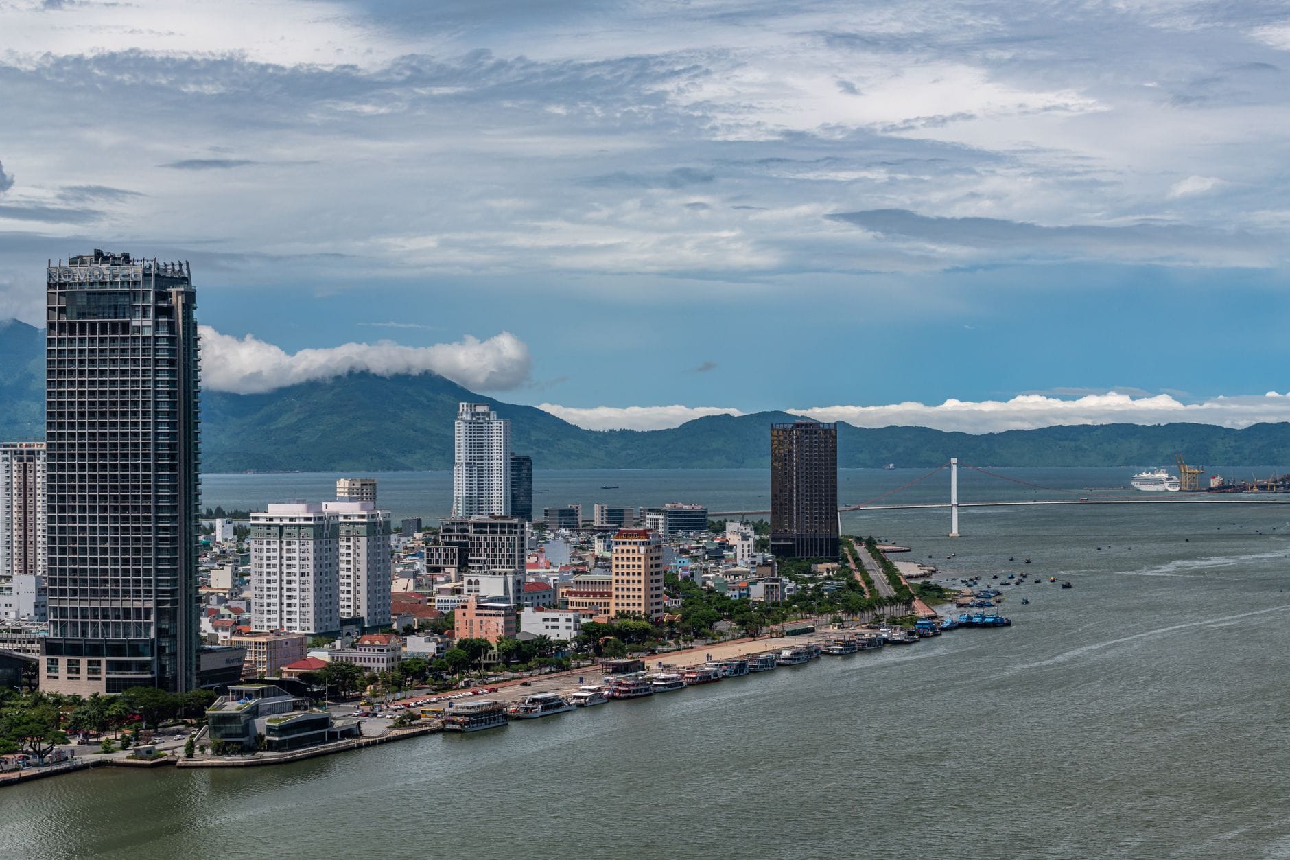 เส้นขอบฟ้าและริมหาดเมืองดานัง ตึกสูง ฉากหลังภูเขา แม่น้ำ ท้องฟ้าสีฟ้า สดใสแบบผสมผสานบรรยากาศเมืองกับธรรมชาติชายฝั่งทะเล