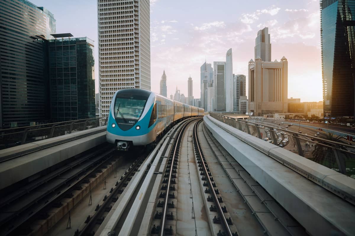 Dubai Metro Zug auf Hochgleisen mit der Stadtsilhouette und modernen Wolkenkratzern im Hintergrund bei Sonnenaufgang oder Sonnenuntergang.