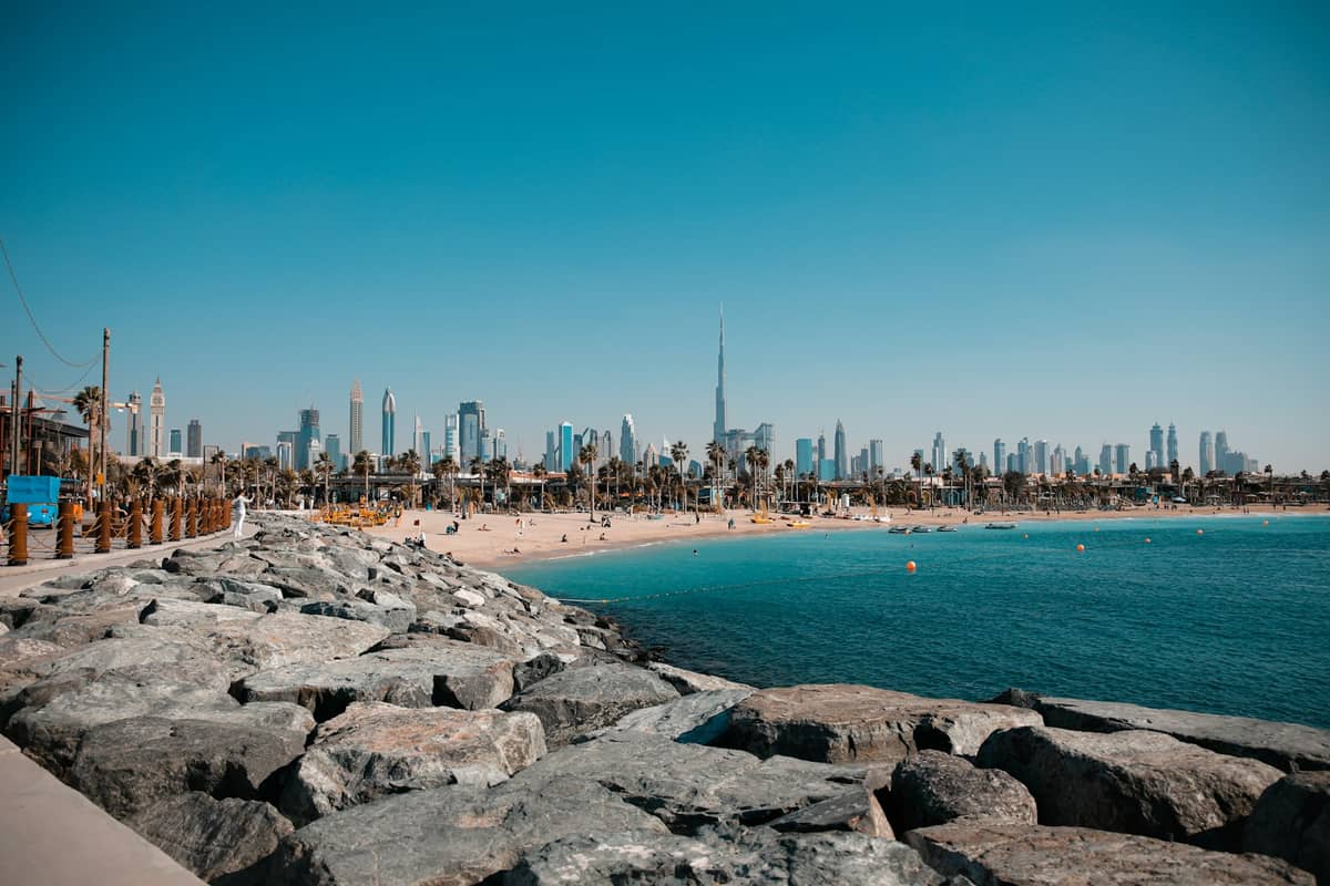 Öffentlicher Strand von Dubai mit klarem blauem Wasser, Palmen und dem Stadtpanorama einschließlich des Burj Khalifa im Hintergrund.