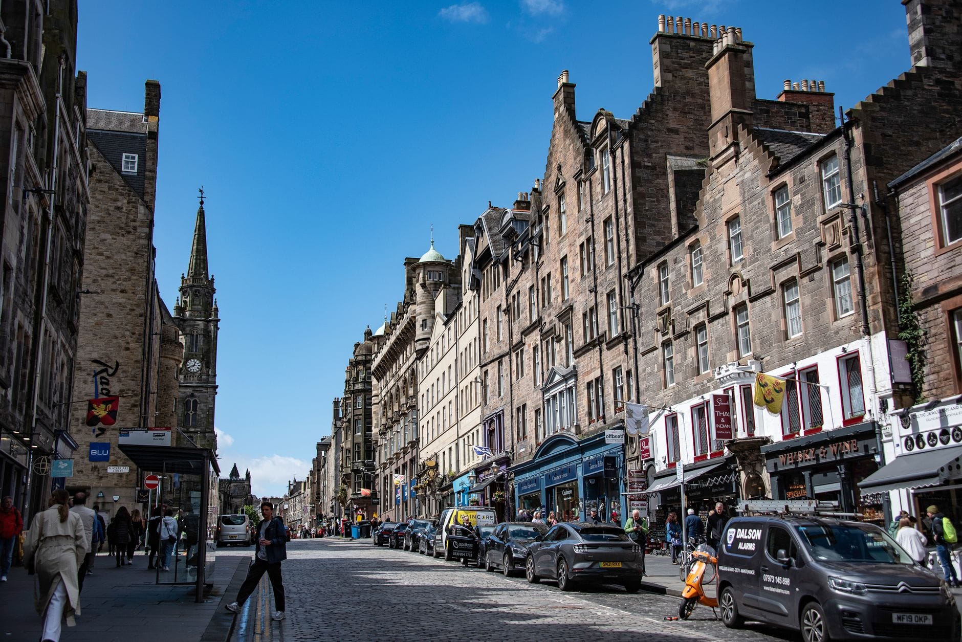 Weiter Blick die gepflasterte Royal Mile hinauf, gesäumt von historischen Steingebäuden, Geschäften und Fußgängern in Edinburghs Old Town.