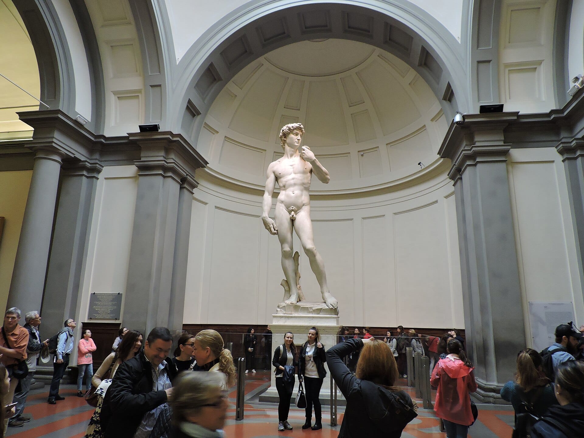 วิวกว้างของรูปปั้น David ของ Michelangelo ภายใน Galleria dell'Accademia ในเมือง Florence พร้อมผู้เข้าชมที่กำลังชื่นชมรูปปั้น