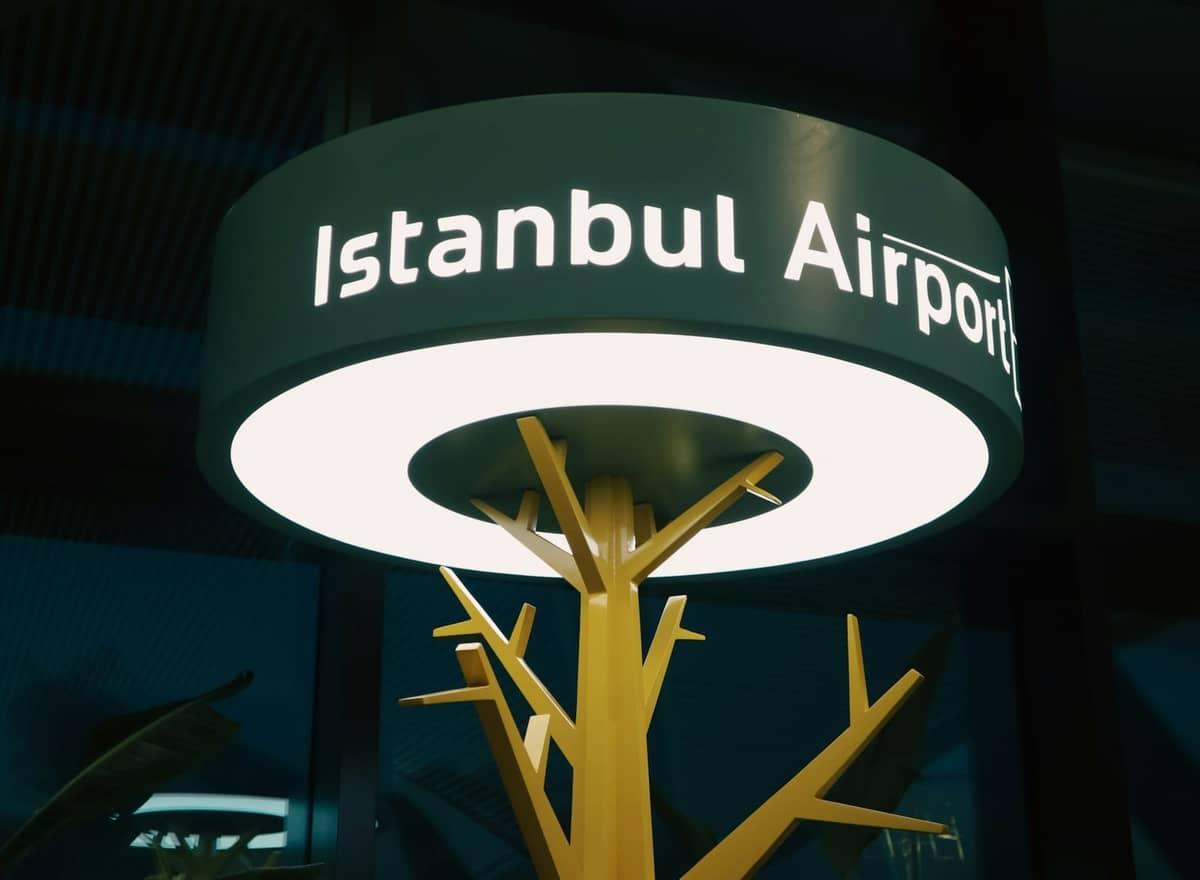 Podświetlony znak Istanbul Airport we wnętrzu, z nowoczesnymi elementami designu i roślinami widocznymi w tle.
