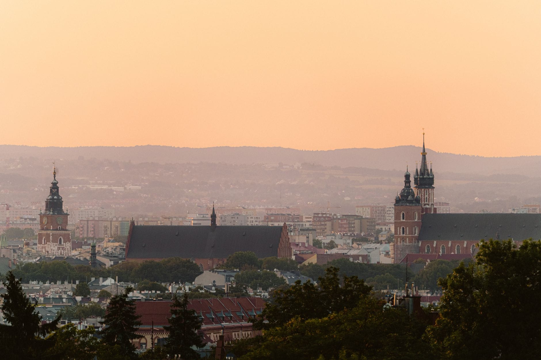 วิวพาโนรามายามพระอาทิตย์ตกของเส้นขอบฟ้าเมือง Kraków ที่มีโบสถ์ประวัติศาสตร์และหลังคาบ้านพร้อมเนินเขาอยู่เบื้องหลัง