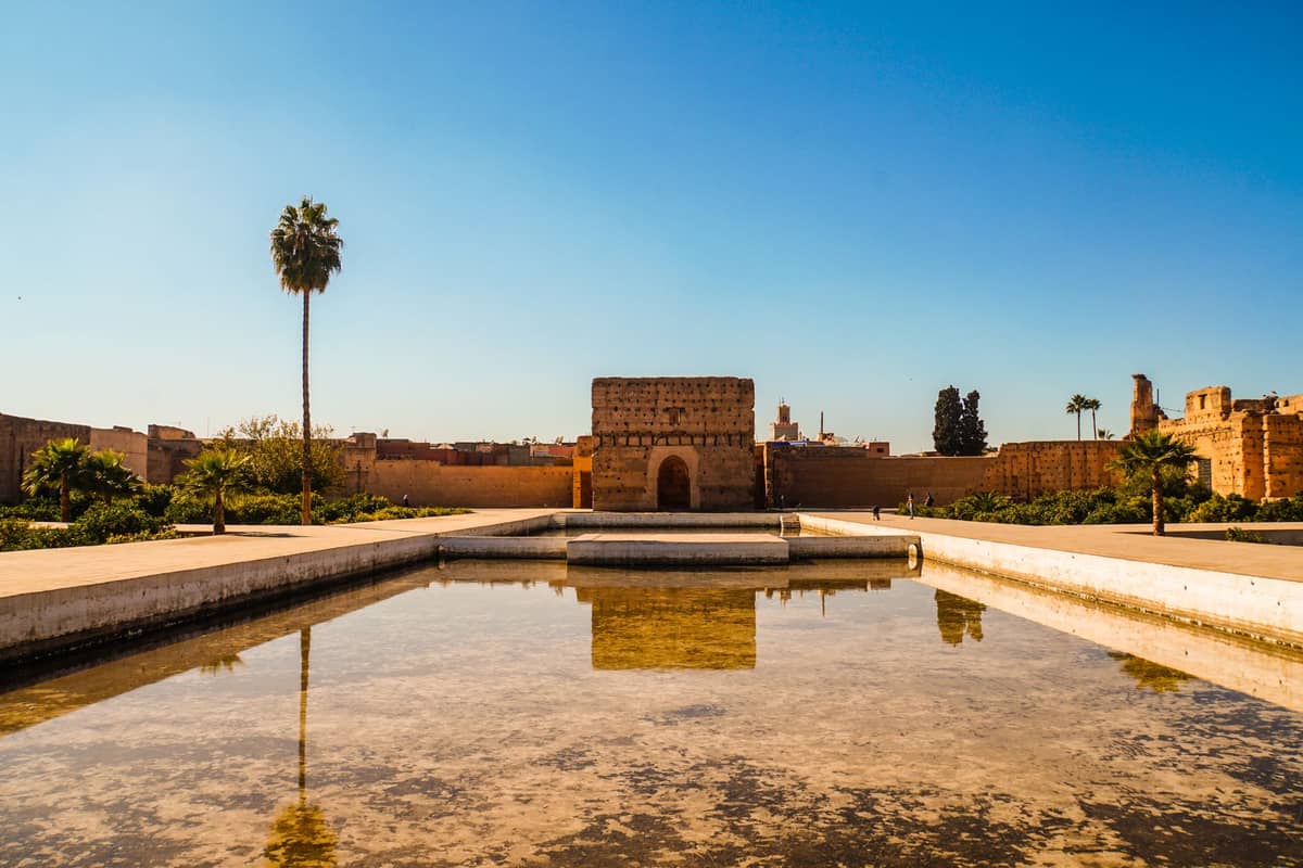 สระน้ำสะท้อนแสงสี่เหลี่ยมขนาดใหญ่ด้านหน้ากำแพงและประตูที่พังทลายของพระราชวัง El Badi ภายใต้ท้องฟ้าสีฟ้าสดใส