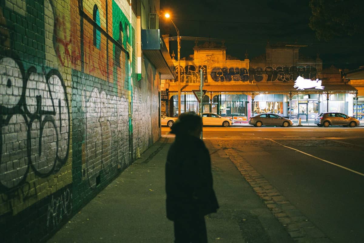 Scène de rue nocturne dans le nord intérieur de Melbourne avec un mur de briques couvert de graffitis et une silhouette sur le trottoir.