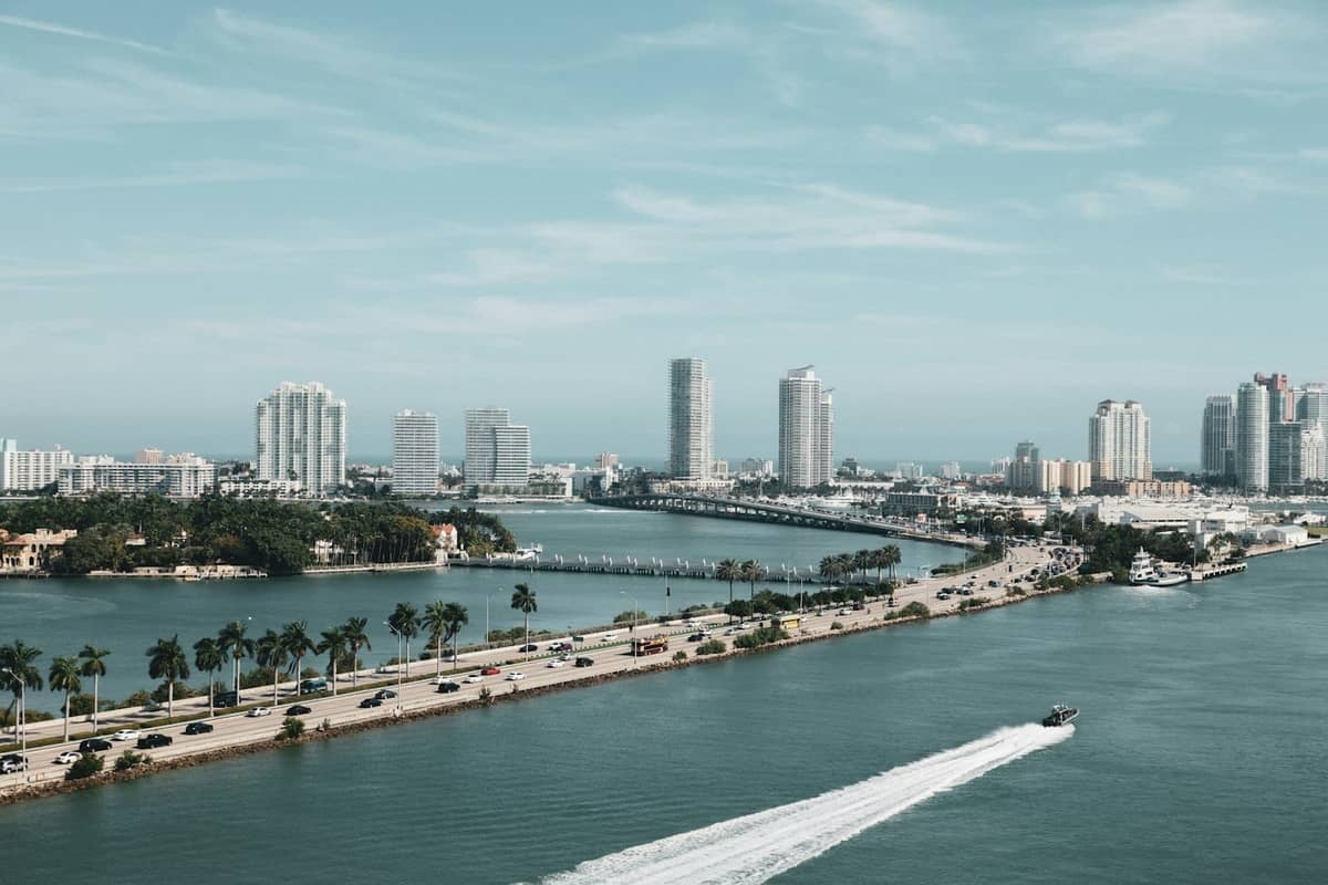 Aerial view of Miami showing a highway connecting the mainland and Miami Beach, with tall buildings and blue water on both sides.