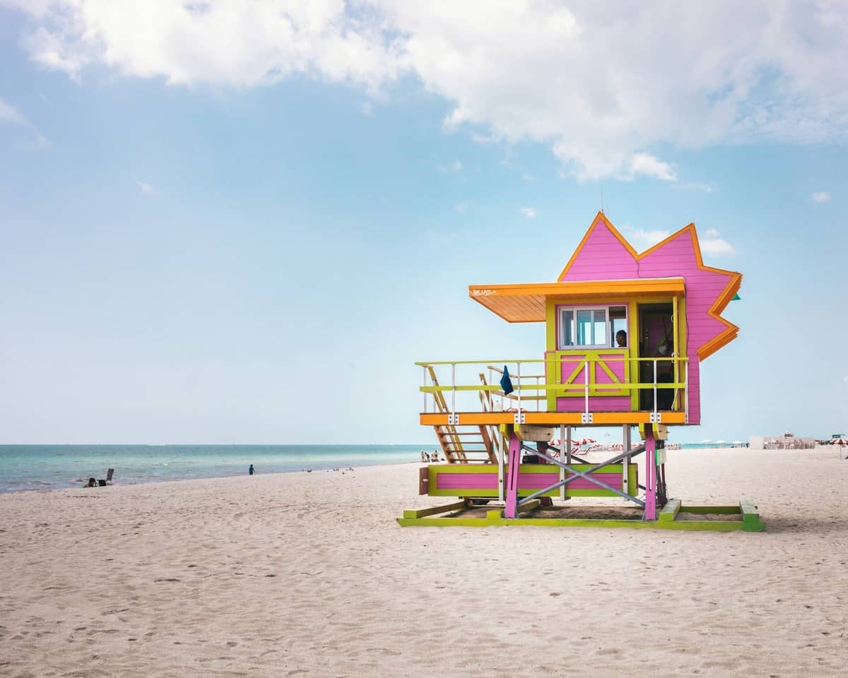 Brightly colored lifeguard tower on sandy South Beach with blue sky and ocean in Miami.