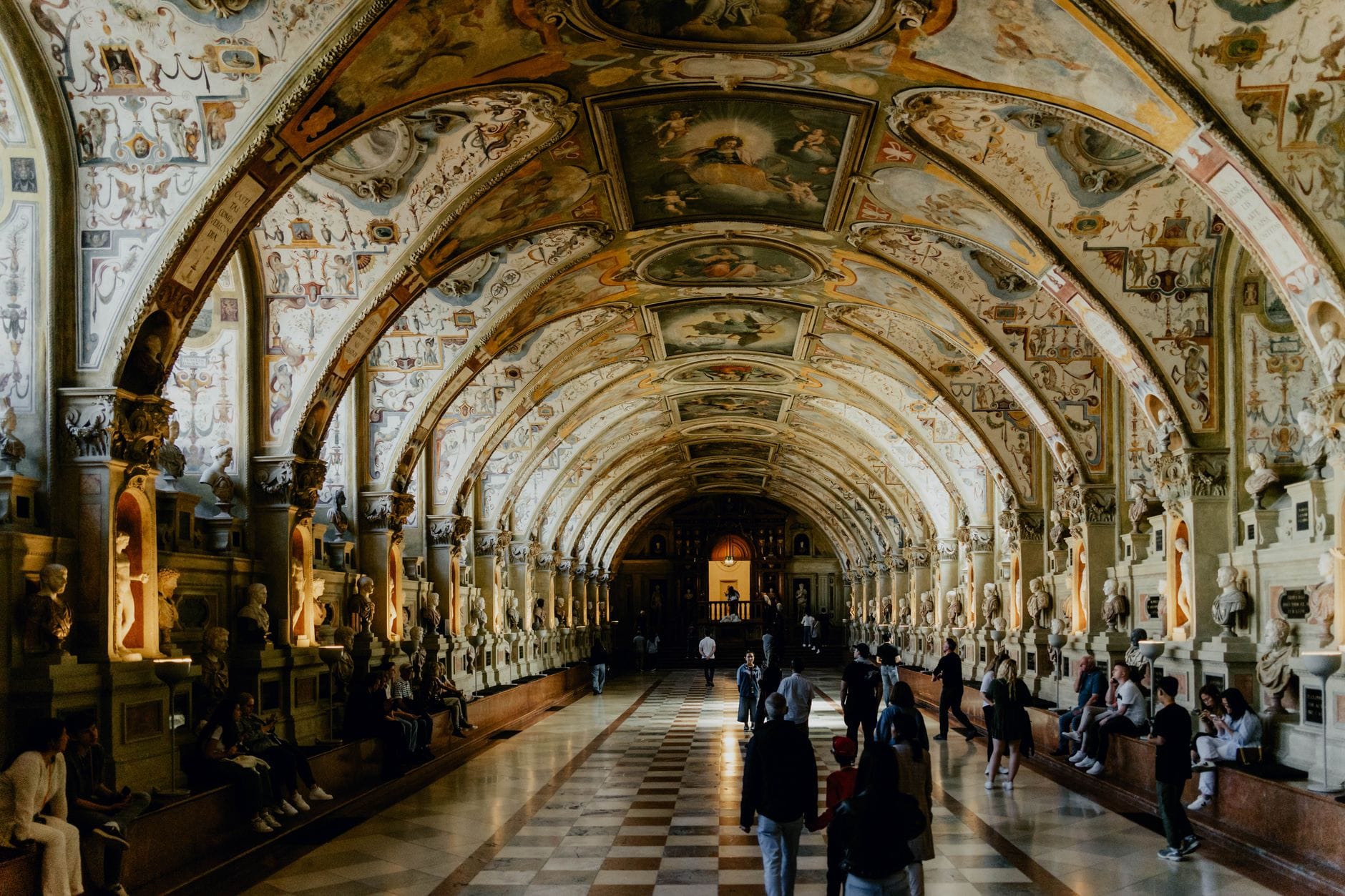 มุมกว้างของห้องโถง Antiquarium สไตล์เรอเนสซองส์อันวิจิตรงดงามใน Munich Residenz เต็มไปด้วยประติมากรรม เพดานประดับตกแต่ง และนักท่องเที่ยวที่เดินชมอยู่ภายใน