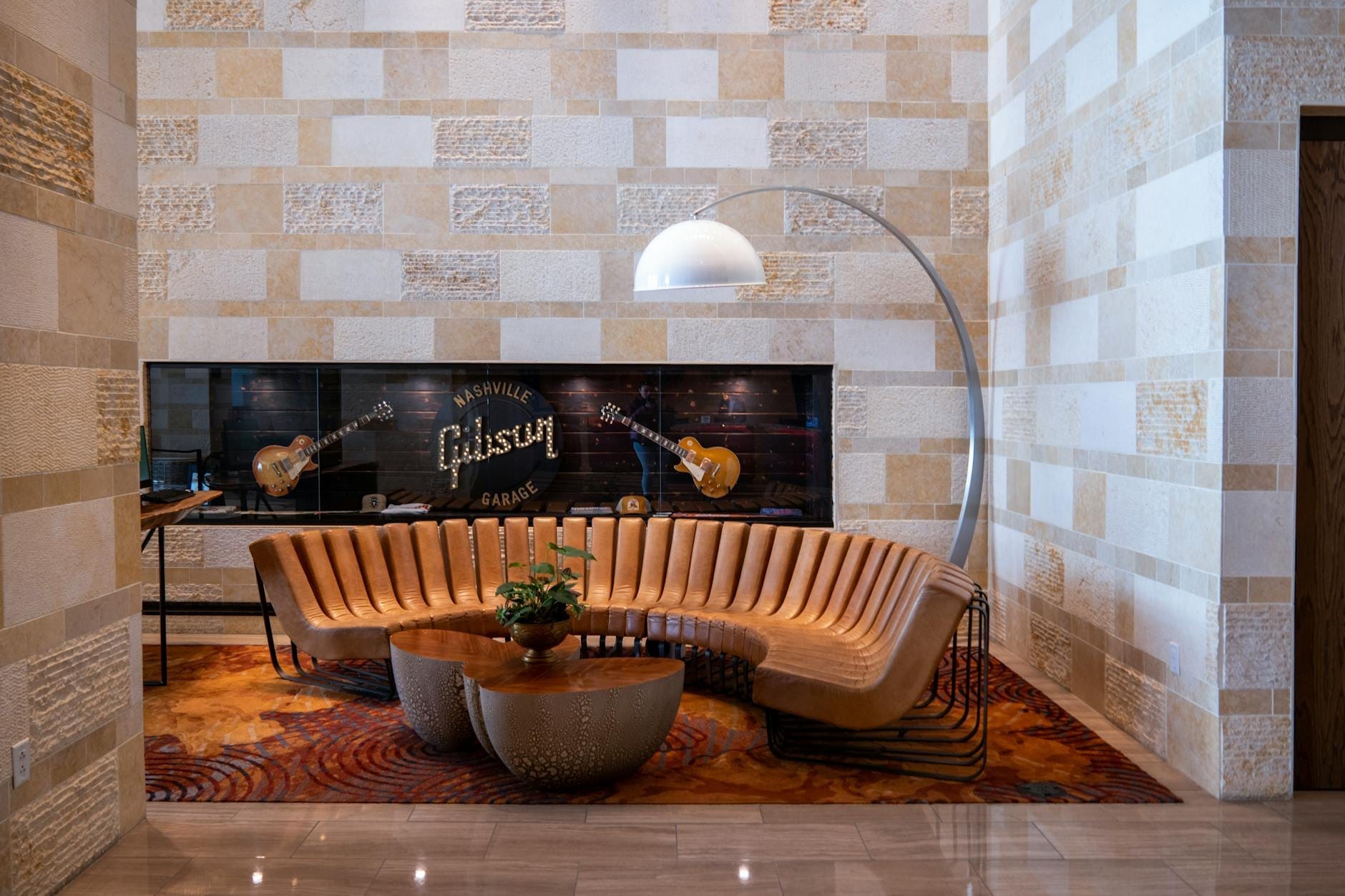 Zona de descanso moderna con un sofá semicircular, guitarras y una exhibición en la pared que dice 'Nashville Gibson' en el interior de un elegante edificio de Nashville.