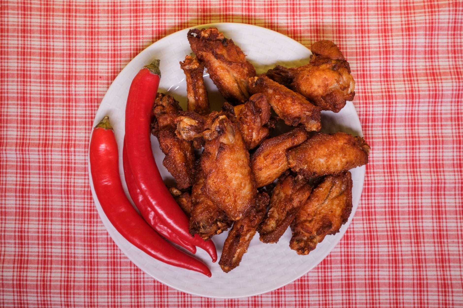 Plato de alitas de pollo frito crujientes y chiles rojos sobre un mantel a cuadros, evocando el clásico Nashville hot chicken.