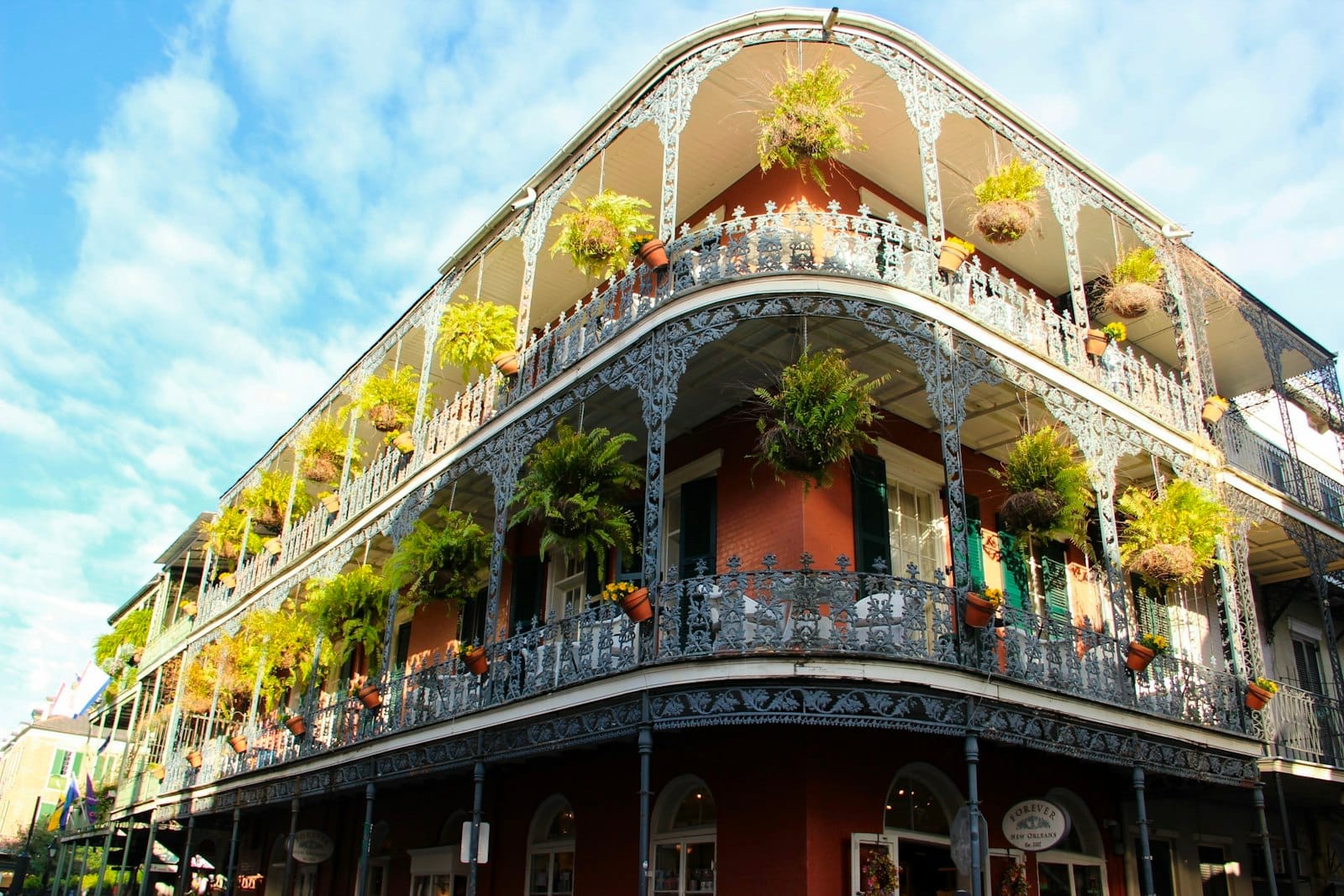 Prédio clássico do French Quarter de Nova Orleans com sacadas de ferro ornamentadas e plantas pendentes exuberantes contra um céu azul intenso, capturando o charme único e a atmosfera da cidade.