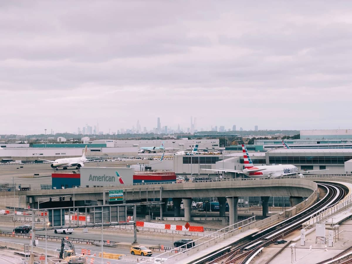 อาคารผู้โดยสารสนามบินพร้อมเครื่องบิน รถไฟยกระดับ และเส้นขอบฟ้าของ New York City ในพื้นหลังใต้ท้องฟ้ามีเมฆ