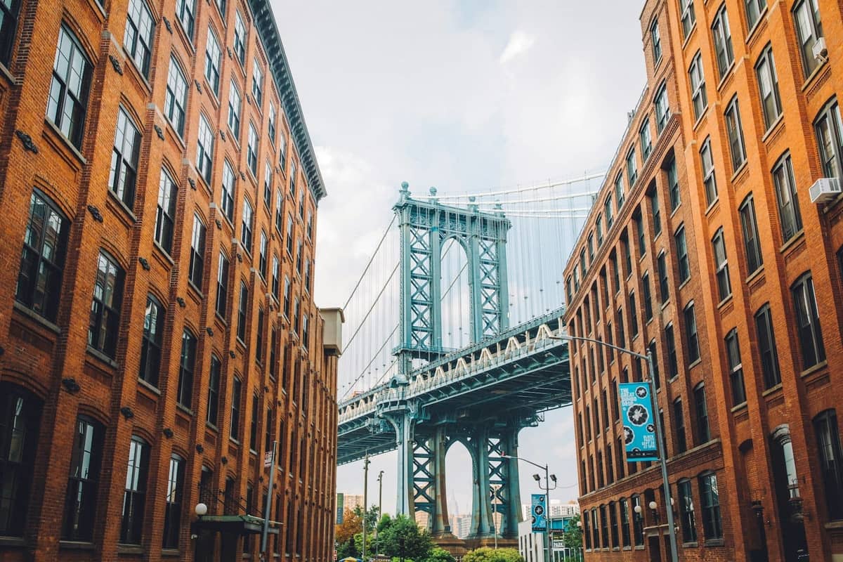 วิวอันโดดเด่นของ Manhattan Bridge ที่ถูกกรอบด้วยอาคารอิฐแดงใน DUMBO, Brooklyn ในวันที่แสงสว่างและท้องฟ้าแจ่มใส