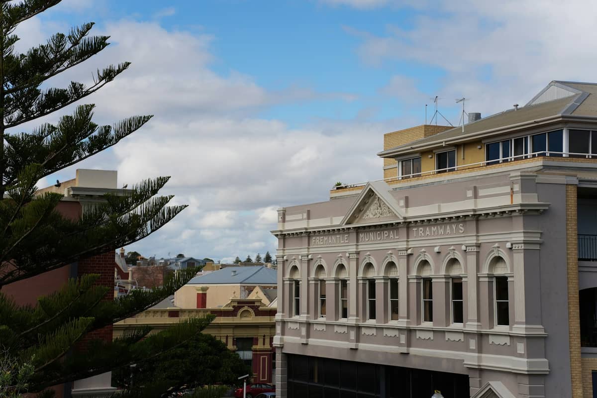 Paisaje urbano de Fremantle con históricos edificios de la época victoriana bajo un cielo parcialmente nublado con árboles en primer plano.