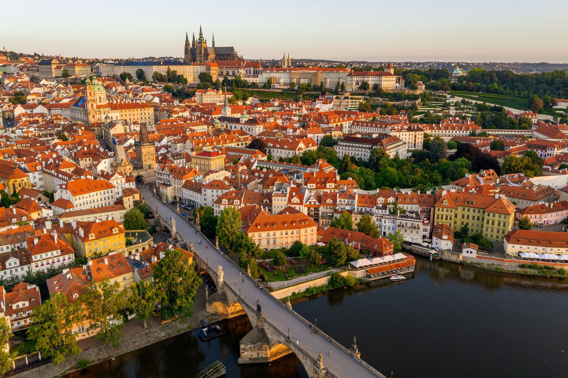 Aerial na tingin ng Charles Bridge, Malá Strana, at Prague Castle sa pagsaluban ng araw na may mga pulang bubong at ilog na Vltava.