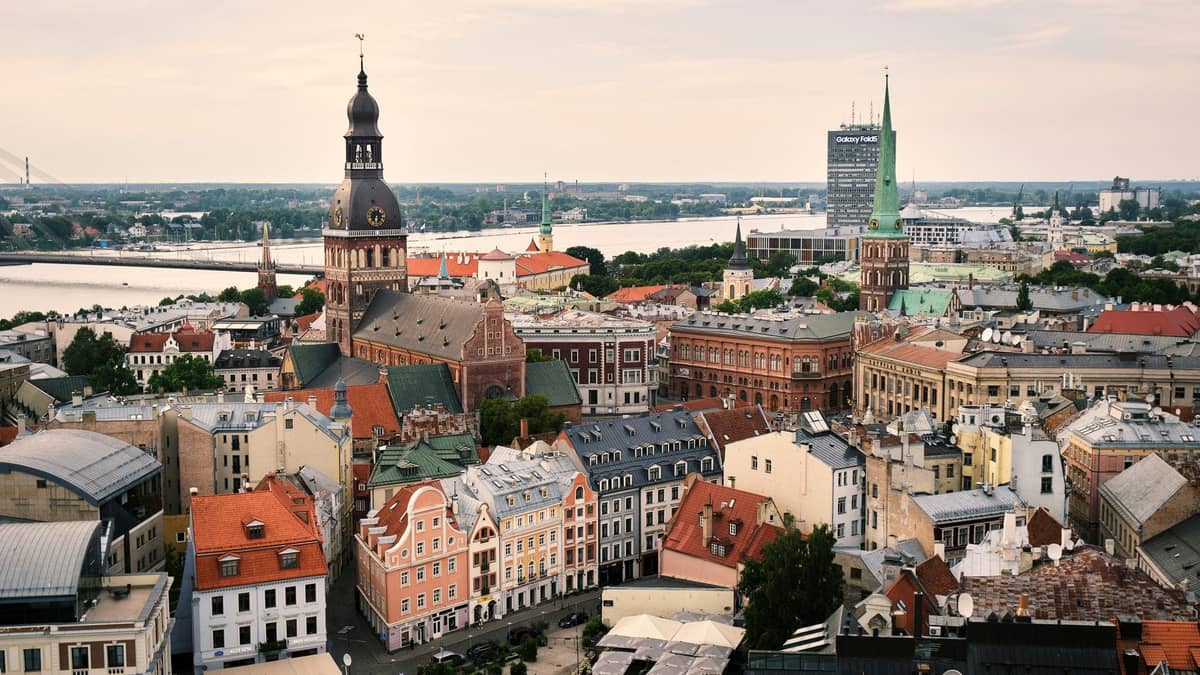Luftaufnahme des mittelalterlichen Kerns der Rigaer Altstadt mit bunten historischen Gebäuden, Kirchturmspitzen und der Daugava im Hintergrund an einem klaren Tag.