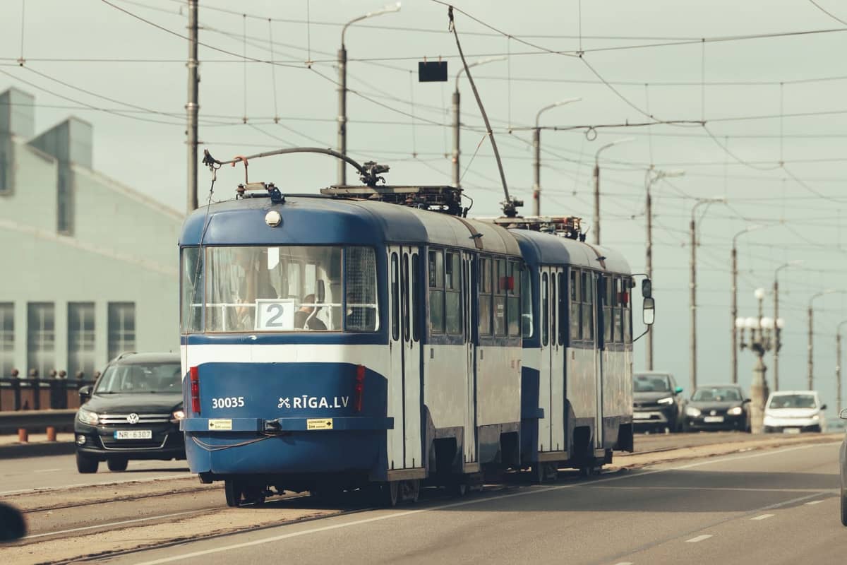 Blau-weiße Straßenbahn aus Riga, die auf einer Stadtstraße neben Autos mit sichtbaren Oberleitungen fährt