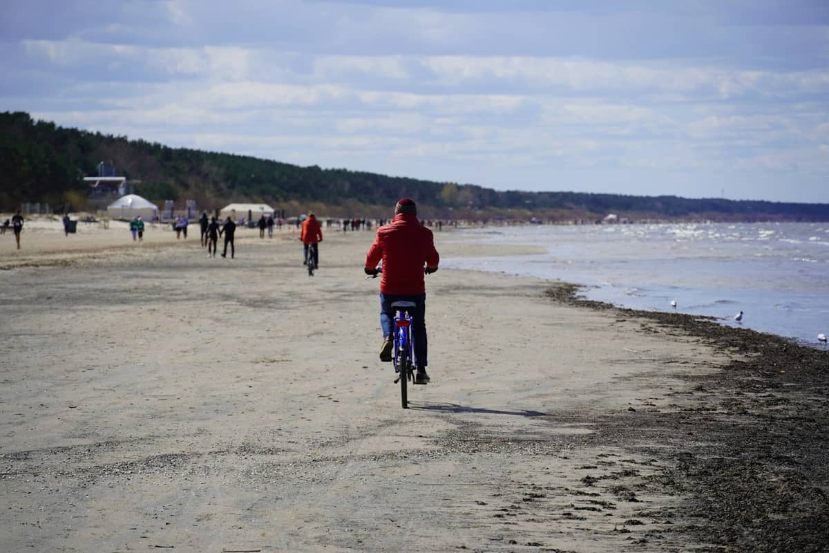 Menschen, die entlang eines Sandstrands mit Kiefernwald spazieren und Fahrrad fahren, typisch für Jūrmala in der Nähe von Riga.