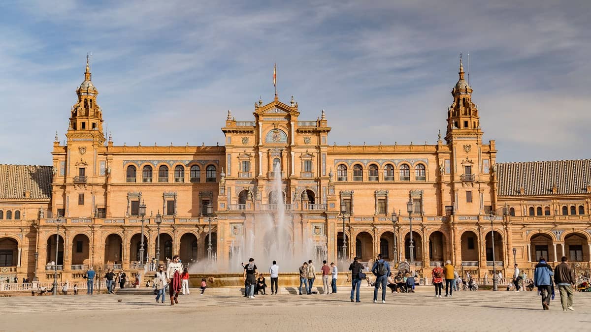 วิวมุมกว้างของ Plaza de España เมืองเซบียา ตึกโค้งน้ำพุใหญ่ หอคอย ผู้คนเดินเล่นในจัตุรัส