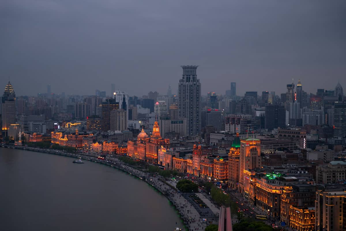 Aerial view of The Bund’s historic waterfront buildings lit up at dusk along the Huangpu River in Shanghai, city skyline in the background.