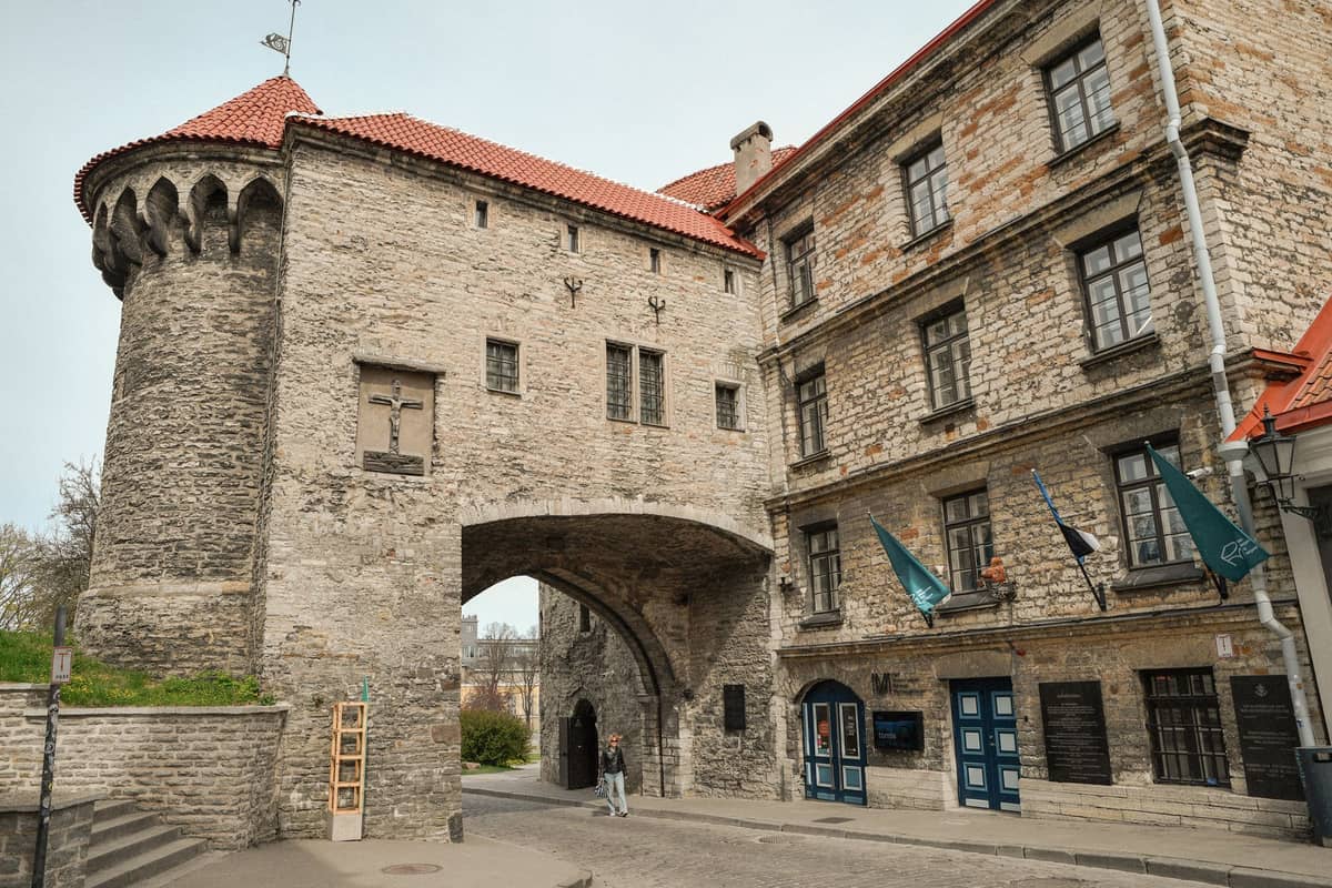 Una puerta de piedra medieval con torreones de tejas rojas y un pasaje arqueado, situada entre edificios históricos en el casco antiguo de Tallinn en una calle tranquila.