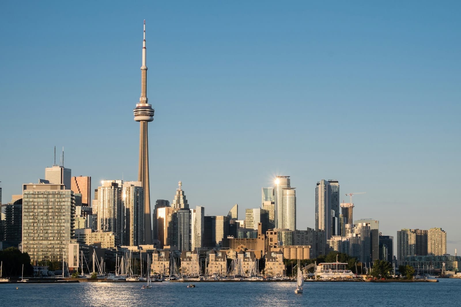 Vista diurna clara do horizonte de Toronto a partir da orla marítima com a CN Tower e edifícios, veleiros ancorados no porto e céu azul.