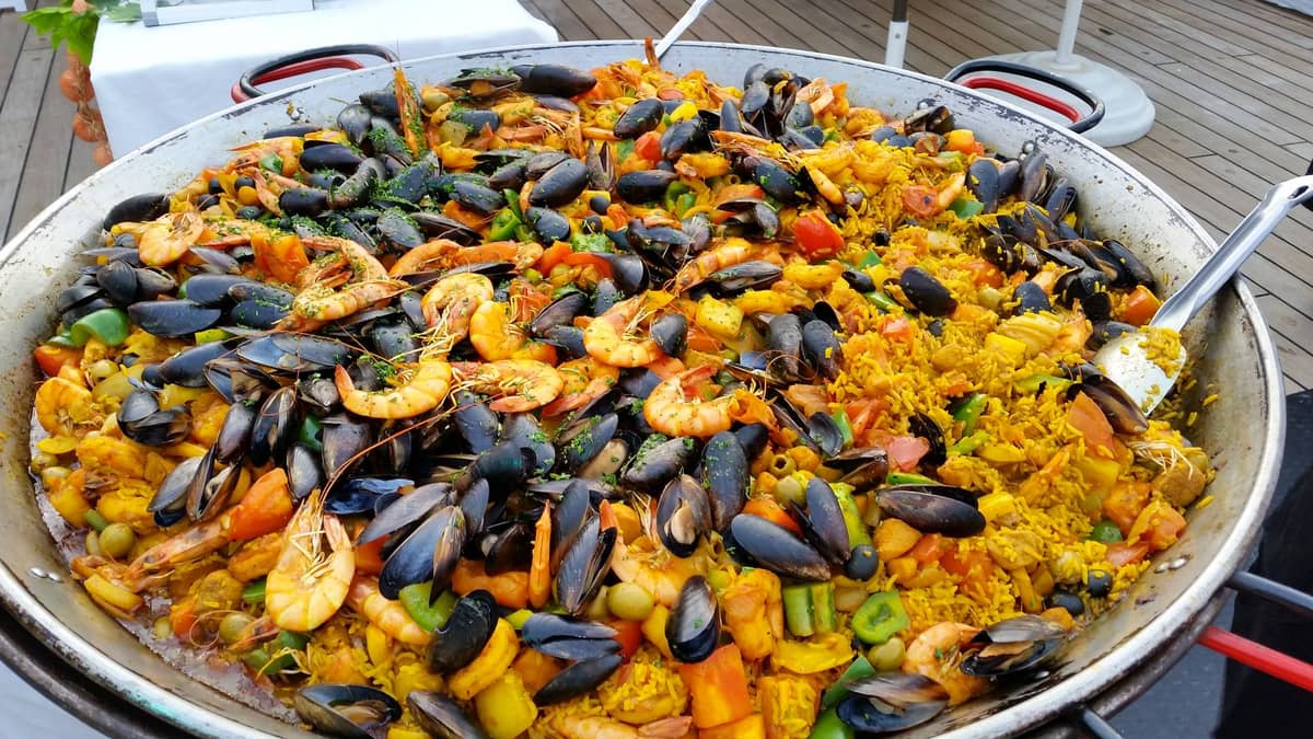 Große Pfanne Meeresfrüchte-Paella mit Garnelen, Muscheln, Gemüse und Reis auf einem Tisch im Freien, typisch für die Küche Valencias.