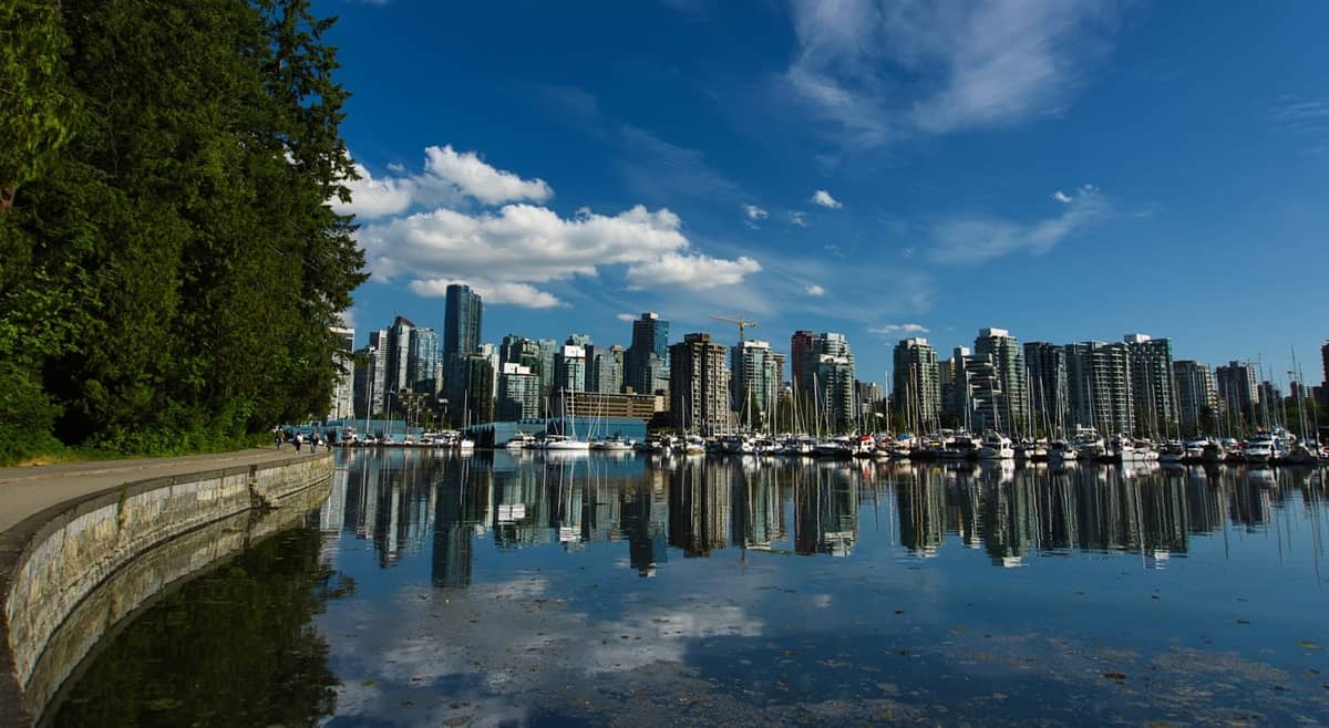 Vancouver Seawall โค้งเลียบ Stanley Park พร้อมตึกระฟ้าใจกลางเมืองและมารีน่าที่สะท้อนในน้ำท่าเรืออันสงบภายใต้ท้องฟ้าสีฟ้า